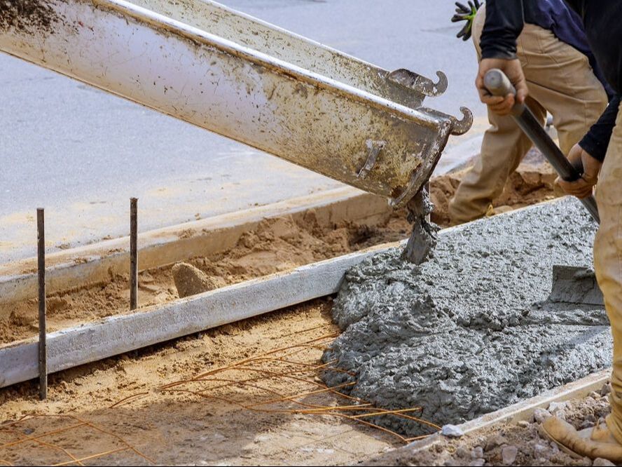 Concrete pouring into a large mold for a sidewalk with concrete contractors spreading.